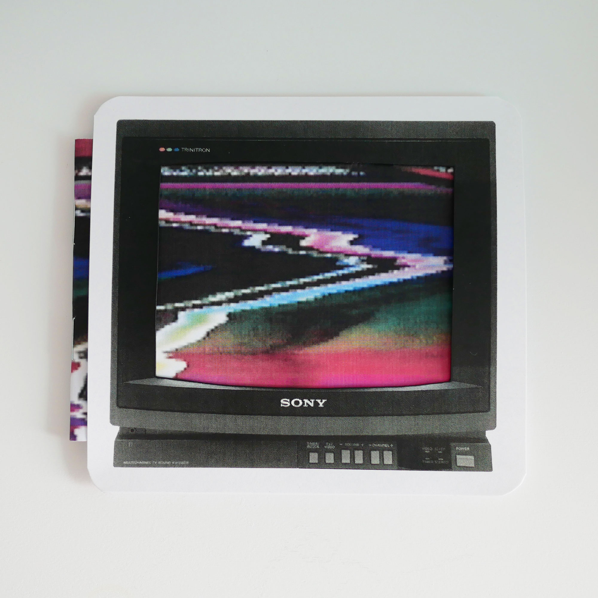 A zine in a TV shaped slipcover with the screen cut out. The booklet cover depicting a scrambled TV image shows through